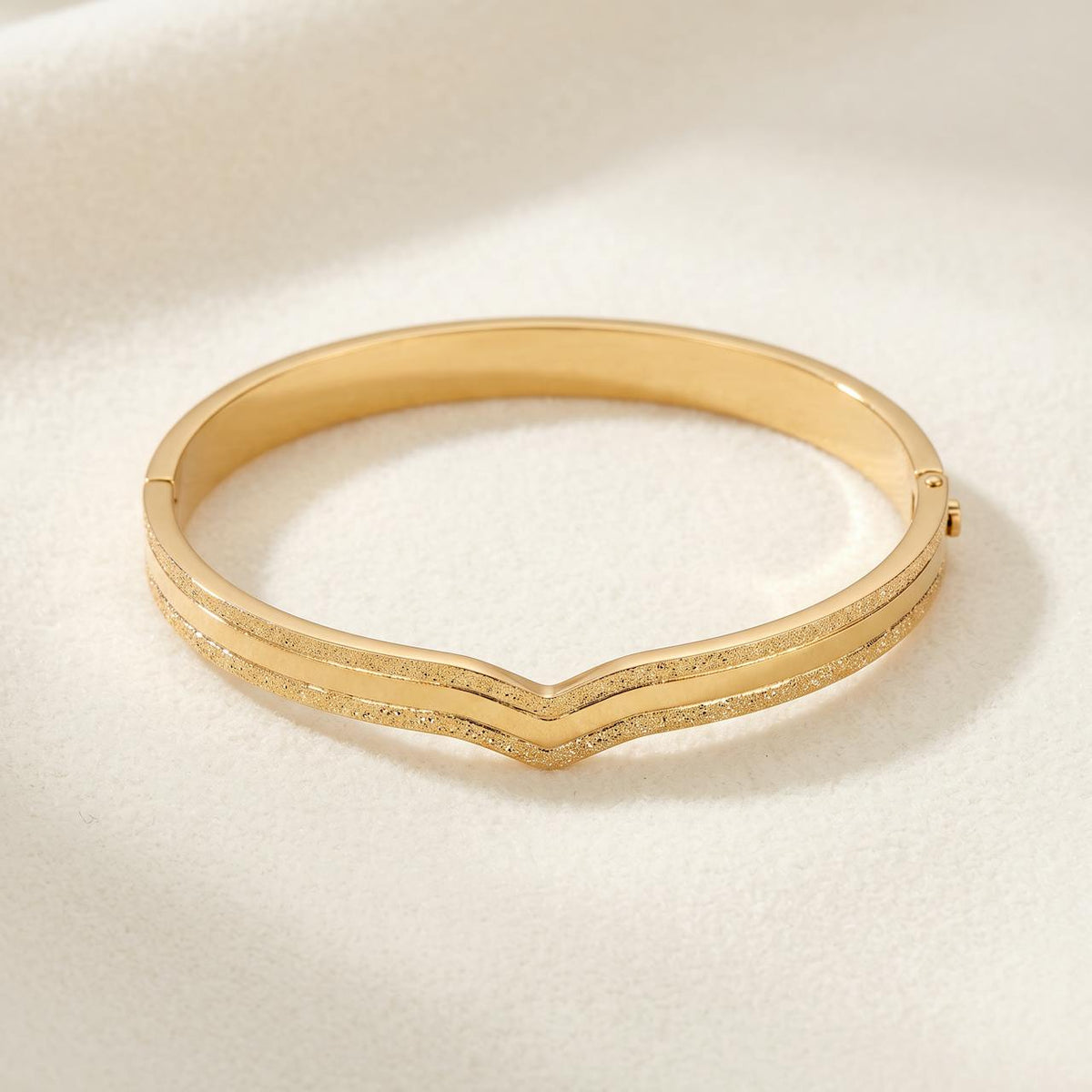 Bracelet jonc doré fermé à bandes ciselées se rejoignant en pointe, sur fond ivoire