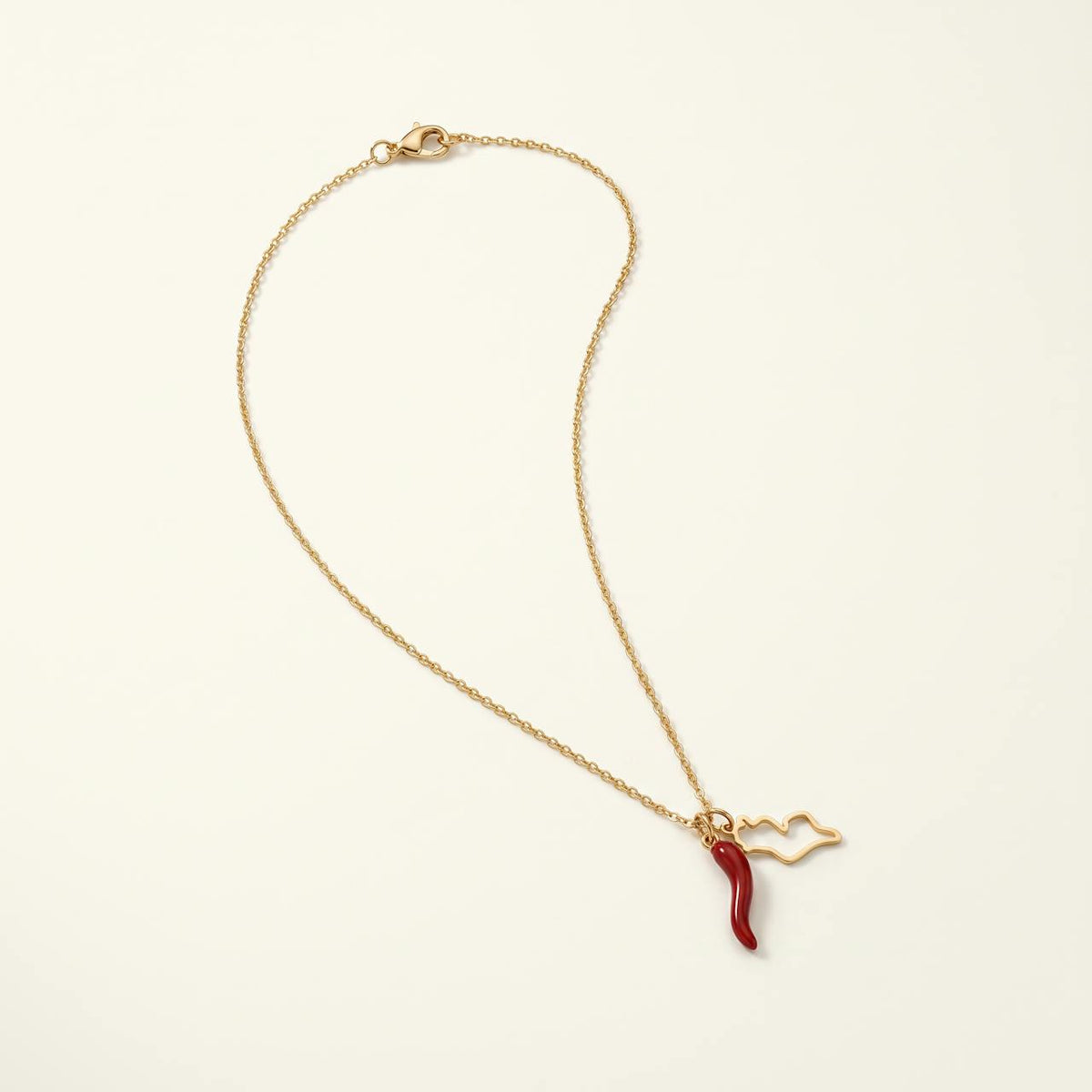 Collier doré avec corne rouge porte-bonheur sur fond ivoire