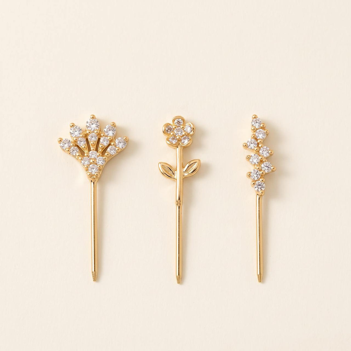 Pack de trois piercings dorés : éventail, fleur sur tige feuillue et grappe, sur fond ivoire
