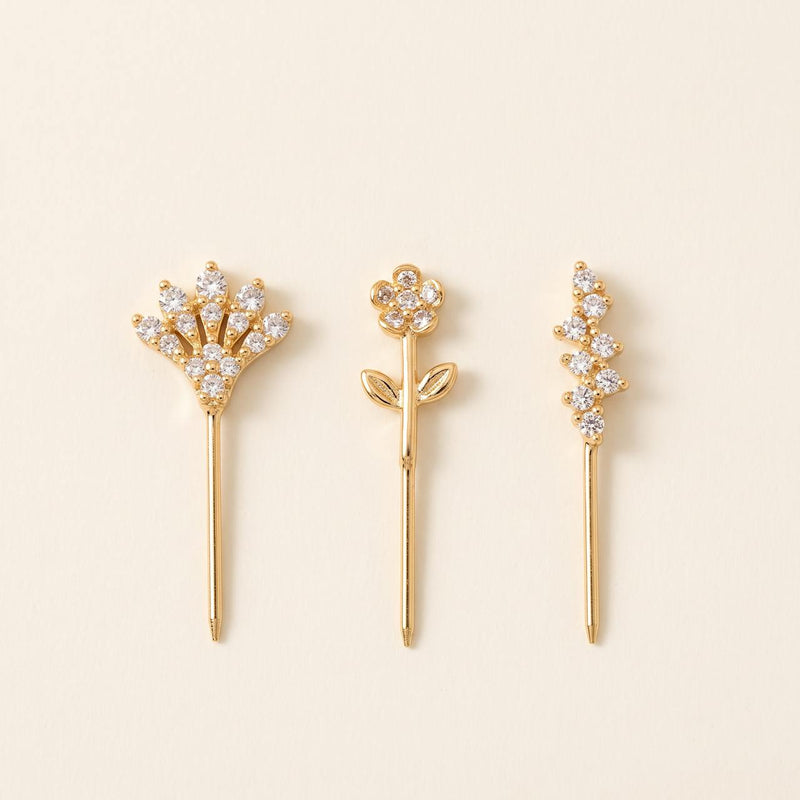 Pack de trois piercings dorés : éventail, fleur sur tige feuillue et grappe, sur fond ivoire