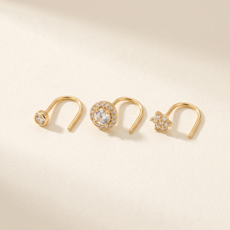 Pack de trois piercings dorés : point lumineux, pastille sertie et fleur, sur fond ivoire