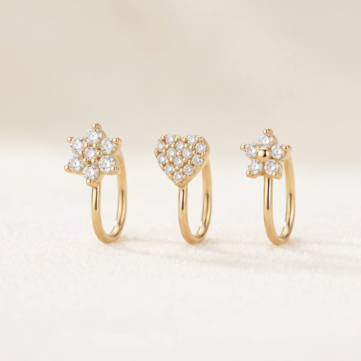 Pack de trois piercings dorés : fleur sertie, cœur pavé et petite fleur, sur fond ivoire