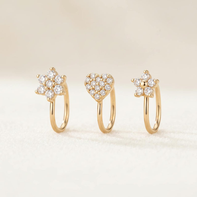 Pack de trois piercings dorés : fleur sertie, cœur pavé et petite fleur, sur fond ivoire